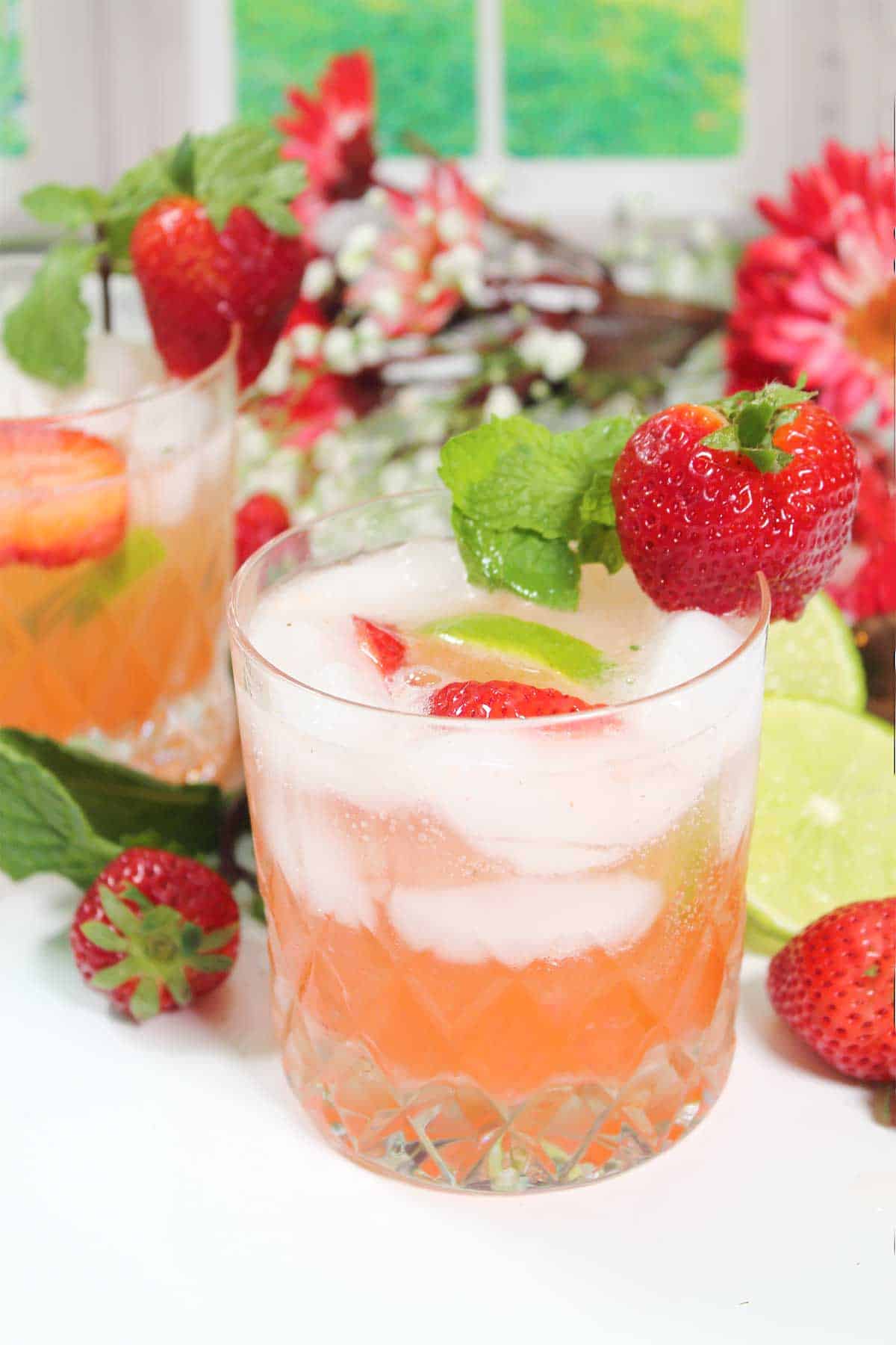 Garnished strawberry mojitos among strawberries and flowers.