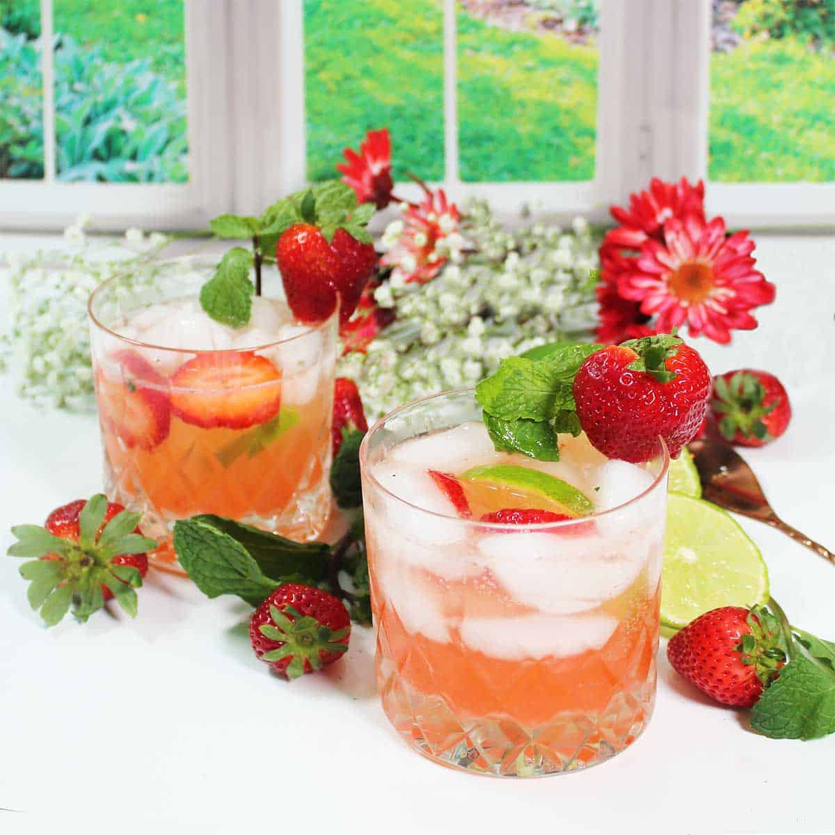 Two garnished strawberry mojito cocktails by garden window.