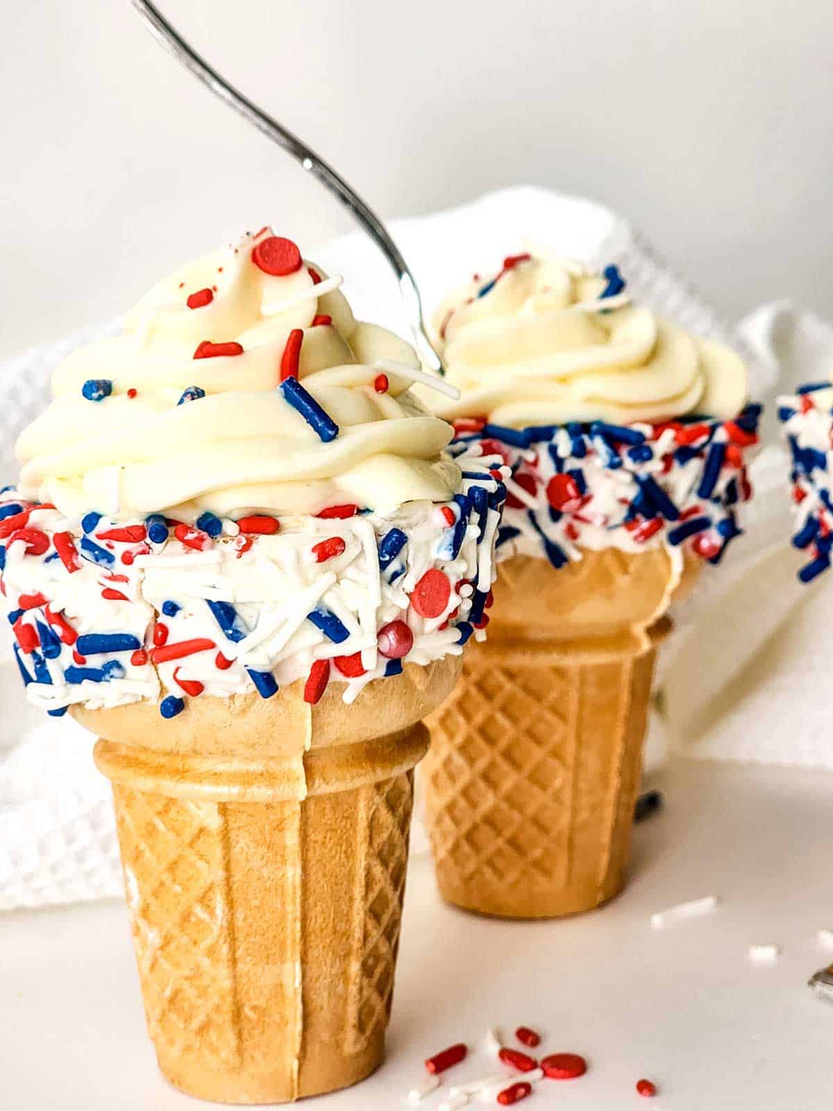 Two filled ice cream cones with cheesecake mousse and covered with red, white and blue sprinkles.