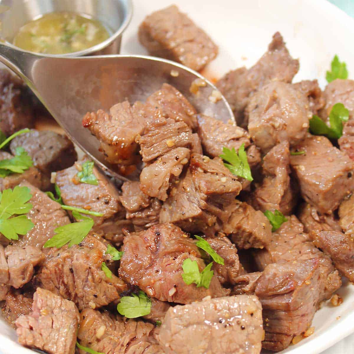 Scooping steak bites out with spoon.
