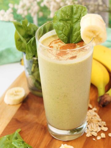 Banana oatmeal smoothie in tall glass on wooden board.