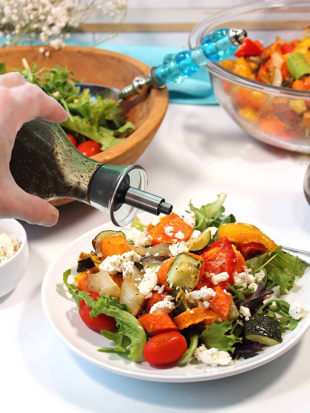 Plated salad topped with roasted vegetables sprinkling on balsamic dressing.