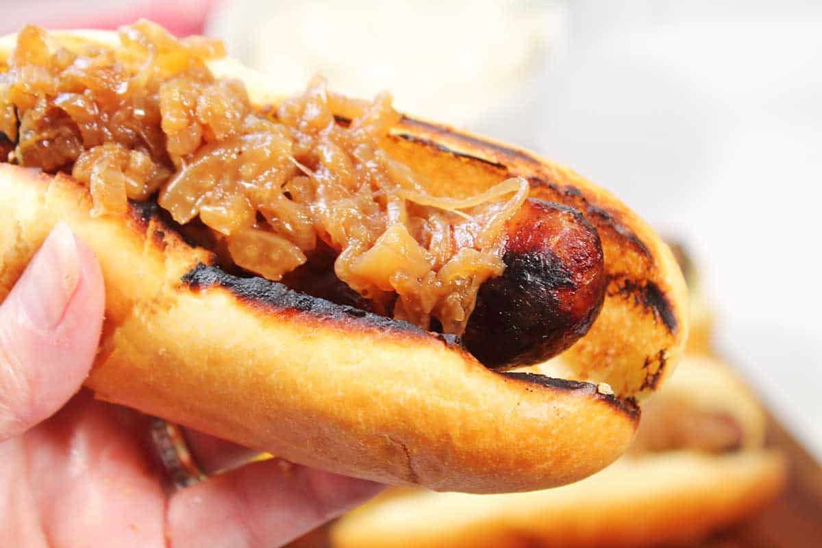 Closeup holding a bratwurst with relish on a bun.