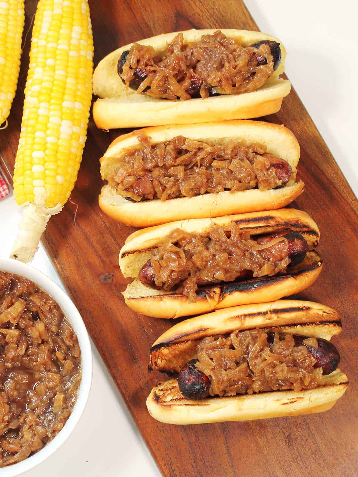 Overhead of grilled brats on rolls topped with caramelized onion and fennel relish.