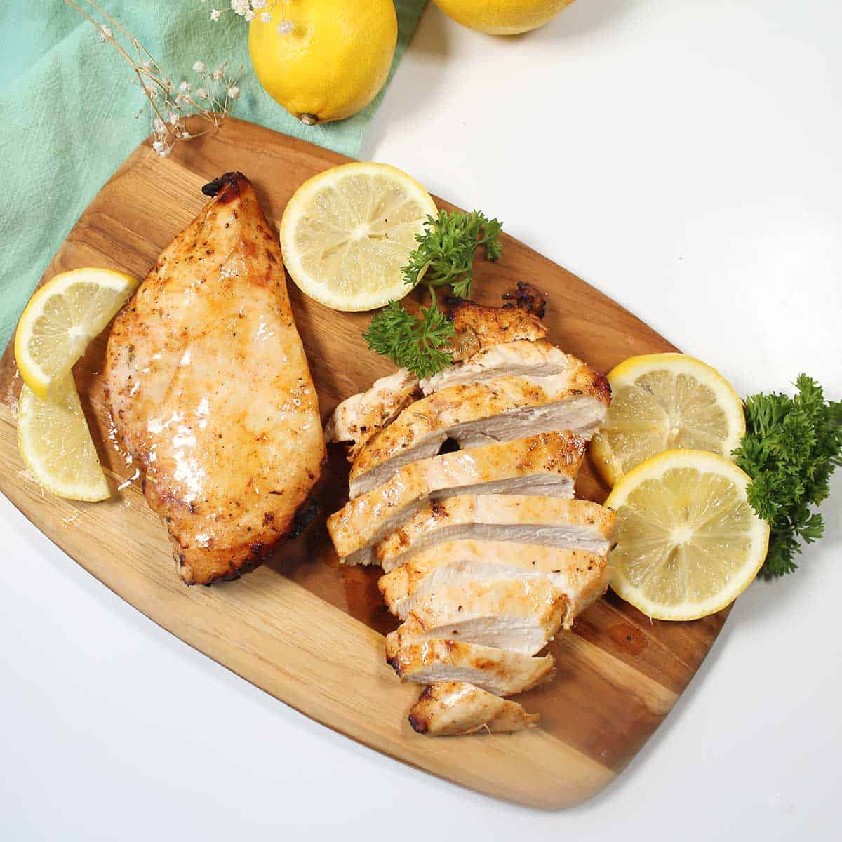 Overhead of chicken breasts on cutting board with lemon slices.