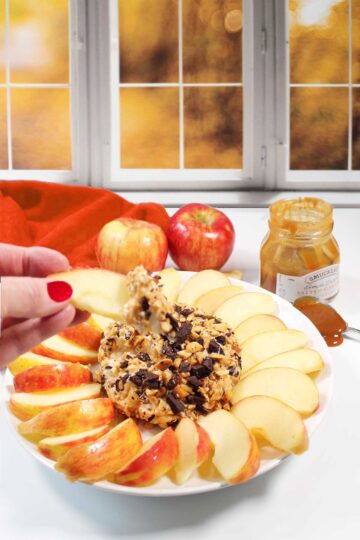 Dipping apple slice in cream cheese dip by fall window.