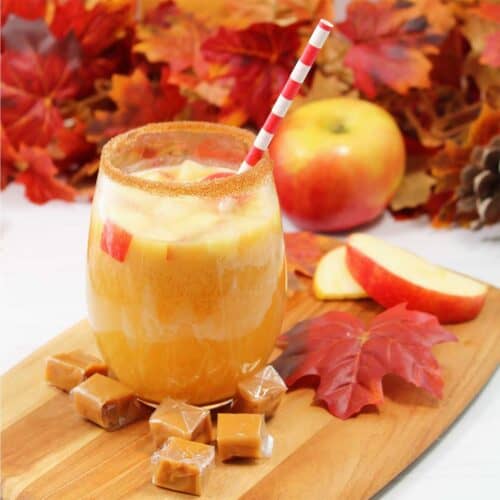 Caramel Apple Sangria in glass with cinnamon sugar rim with fall leaves in back.