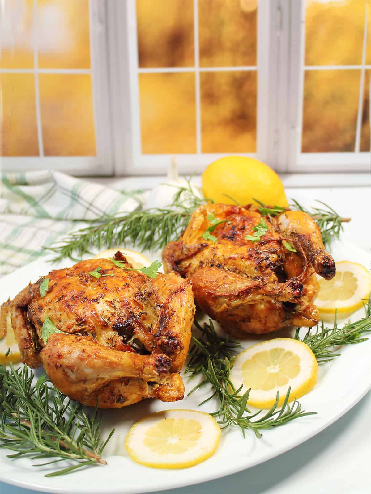 Two air fryer Cornish hens on platter with lemons.