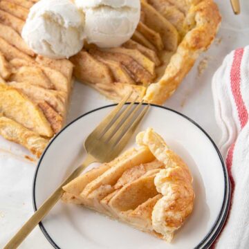 Slice of galette on plate with whole puff pastry with apples beside it.