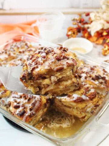 Lifting serving of cinnamon roll french toast out of casserole.