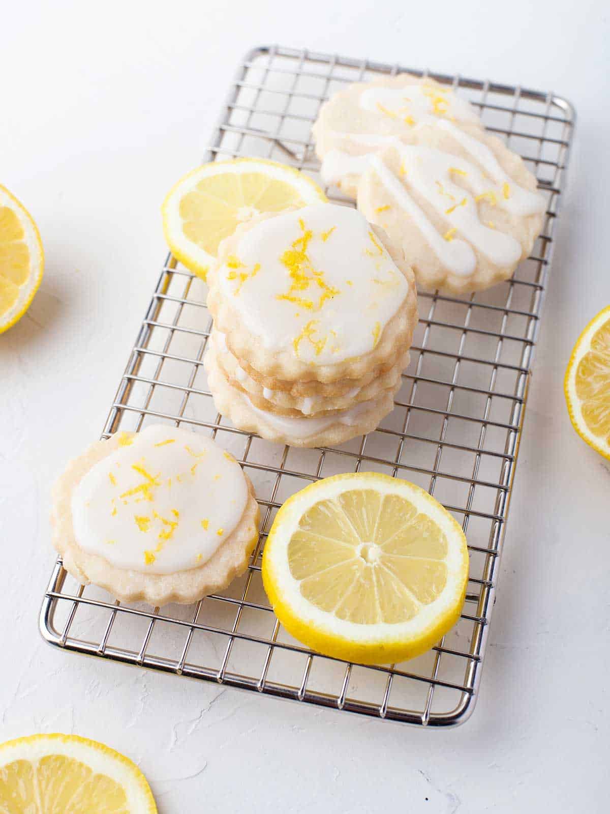 Lemon shortbread cookies stacked on wire rack with lemons.