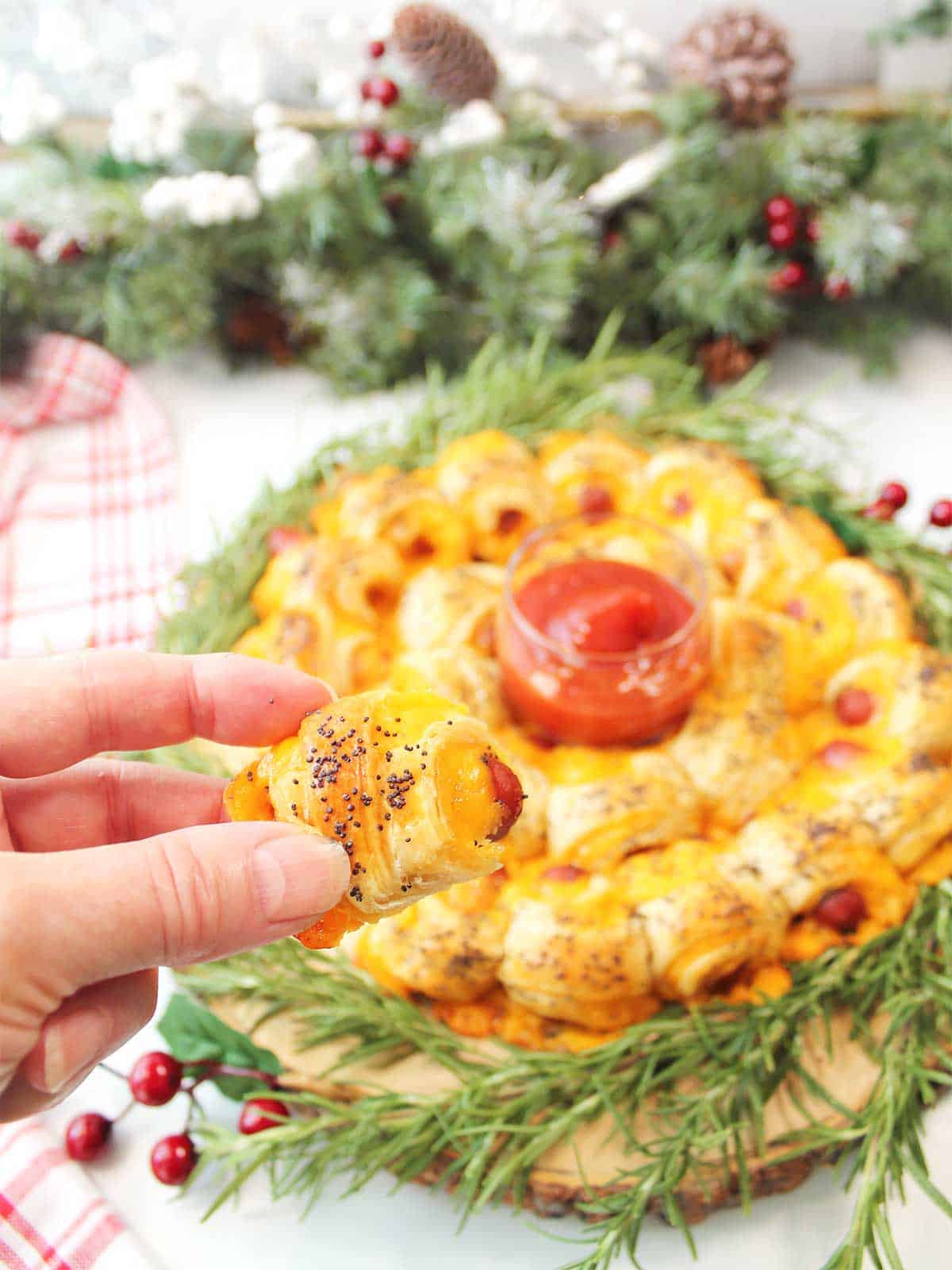 Holding crescent roll wrapped little smokie above wreath.