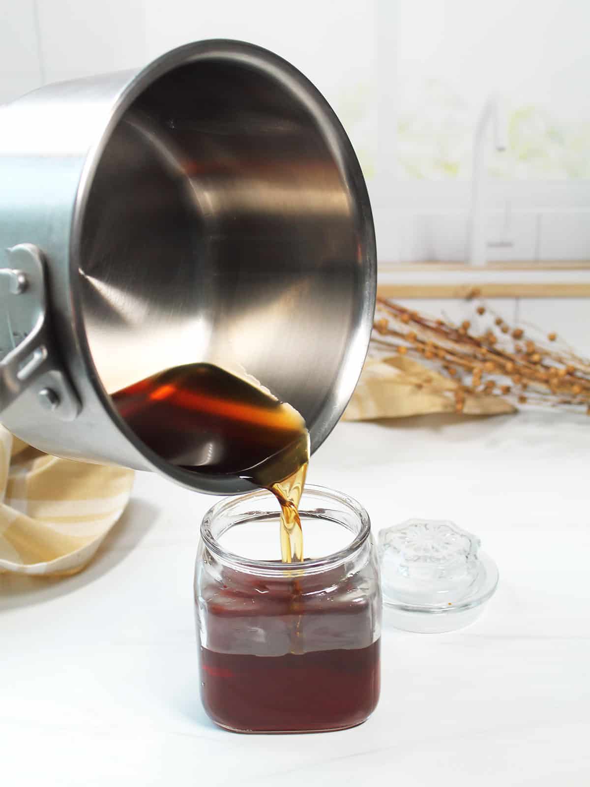 Pouring brown sugar syrup into glass jar.