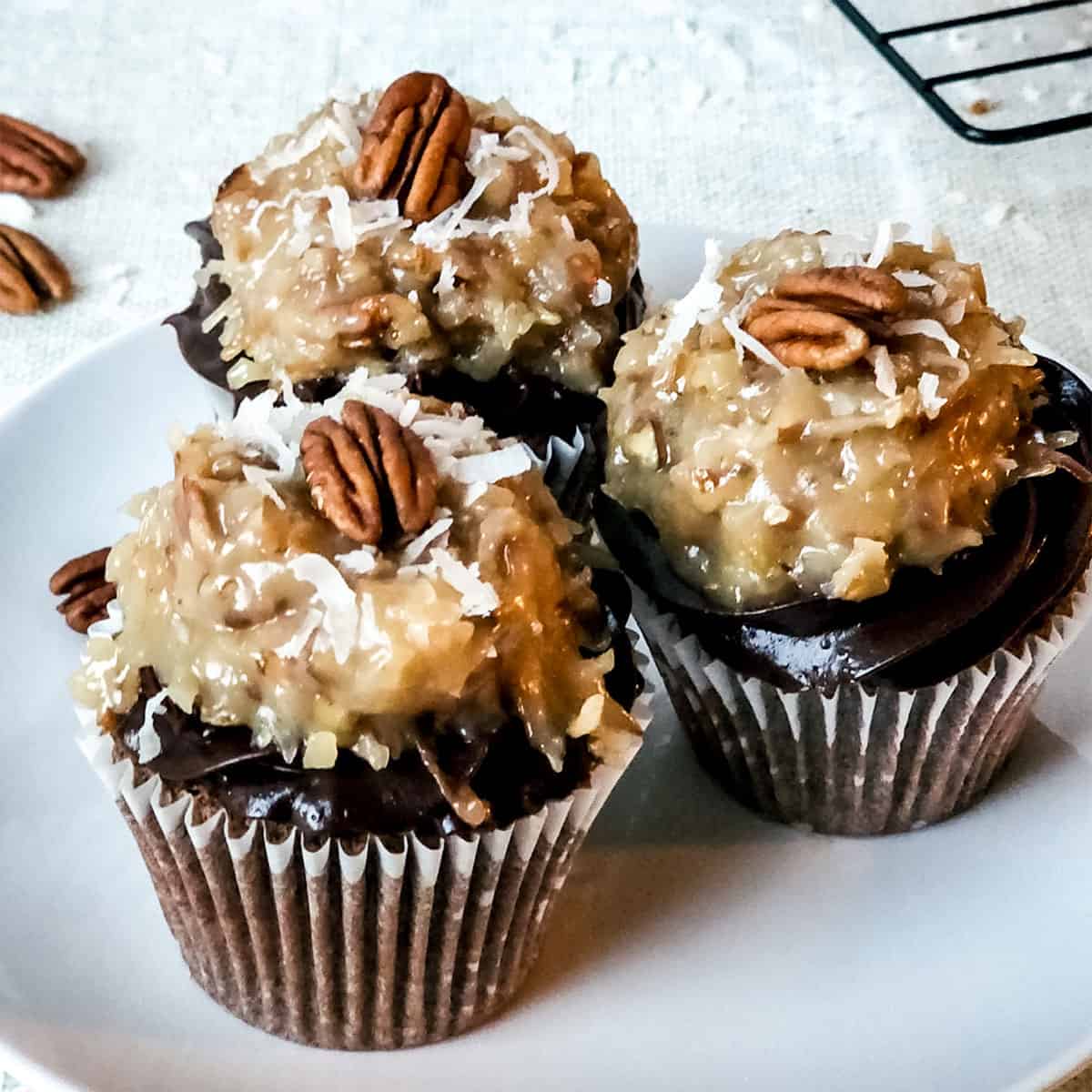 Three German chocolate cake cupcakes with chocolate ganache and coconut pecan topping.