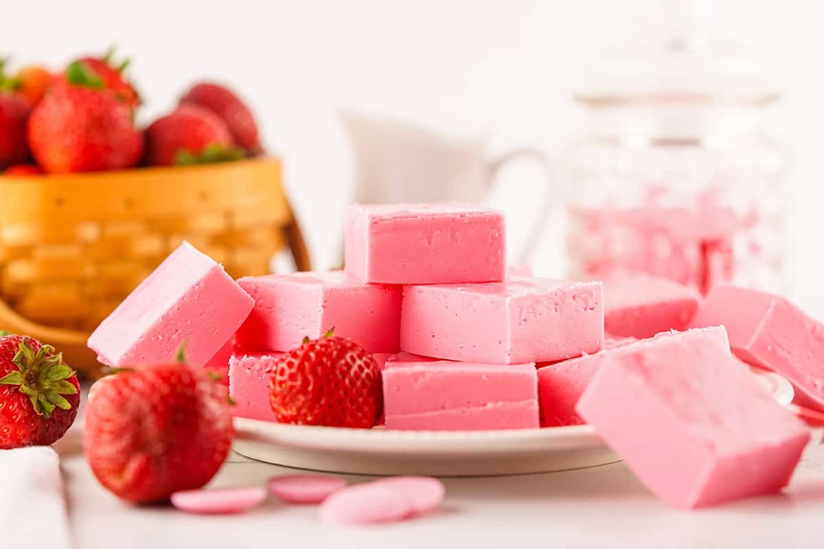 Fudge on a plate with strawberries with basket of strawberries in back.