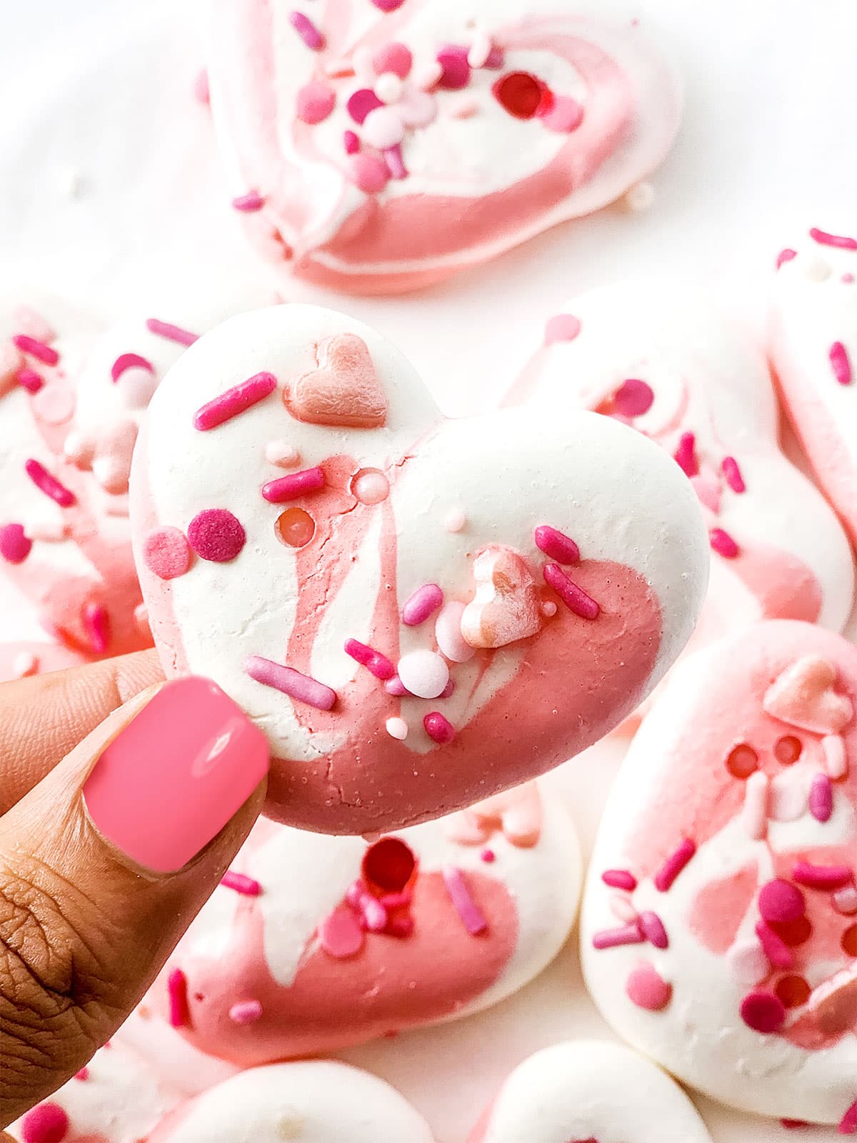 Holding pink and white meringue cookie.