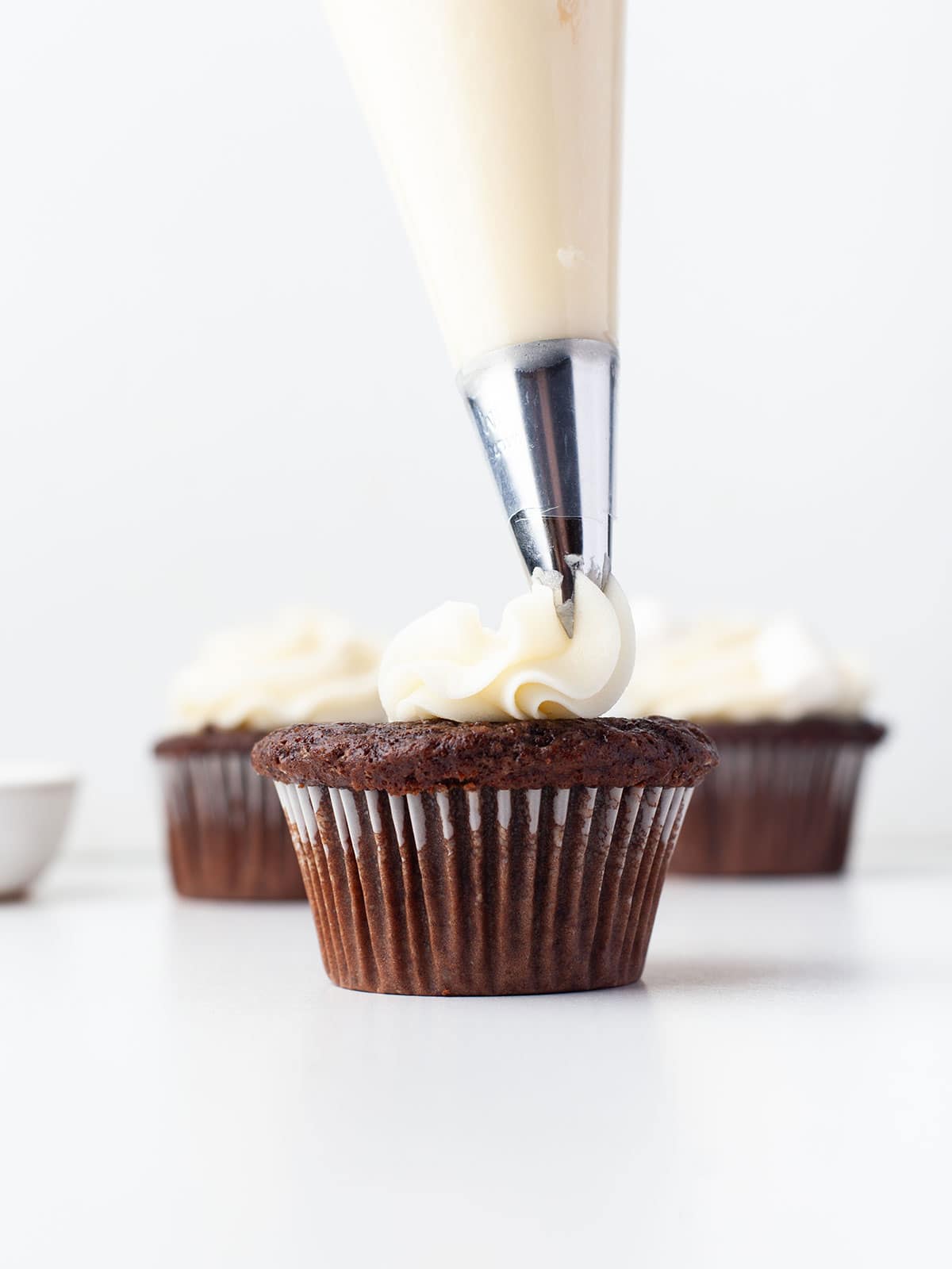 Piping the frosting onto chocolate cupcake.