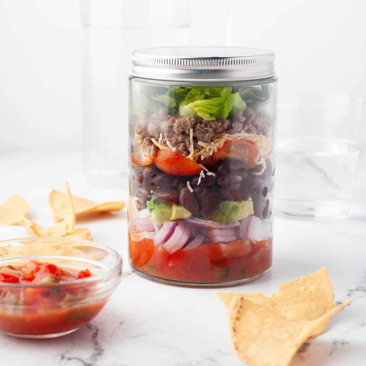 https://2cookinmamas.com/wp-content/uploads/2023/12/Taco-Salad-in-a-jar-with-lid-on-square.jpg