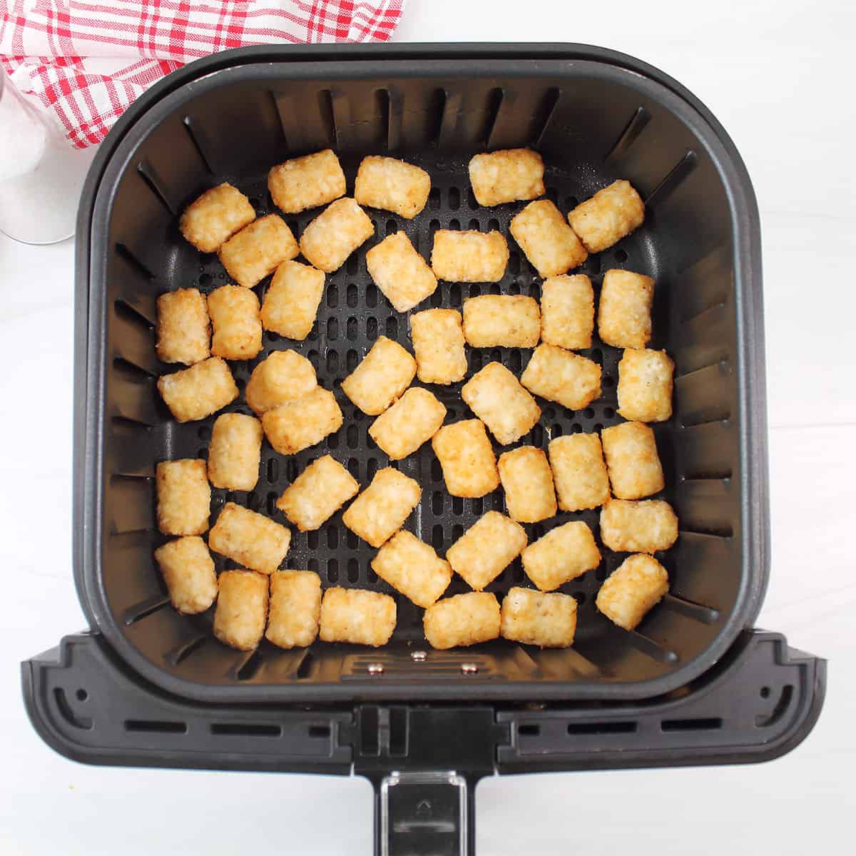 Frozen tots in air fryer basket.