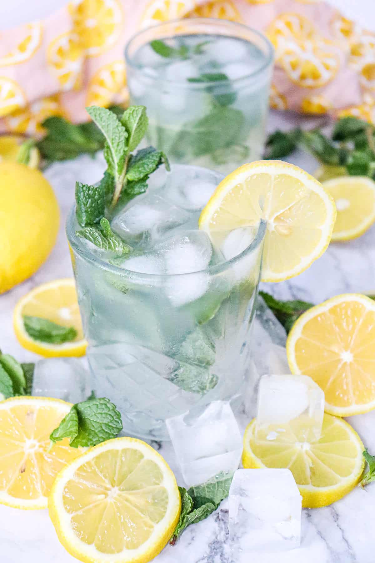 Two lemon mojito mocktails surrounded by lemons and mint.