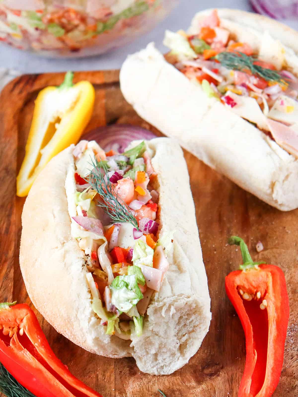 Two chopped Italian Sandwiches on wooden board with peppers.