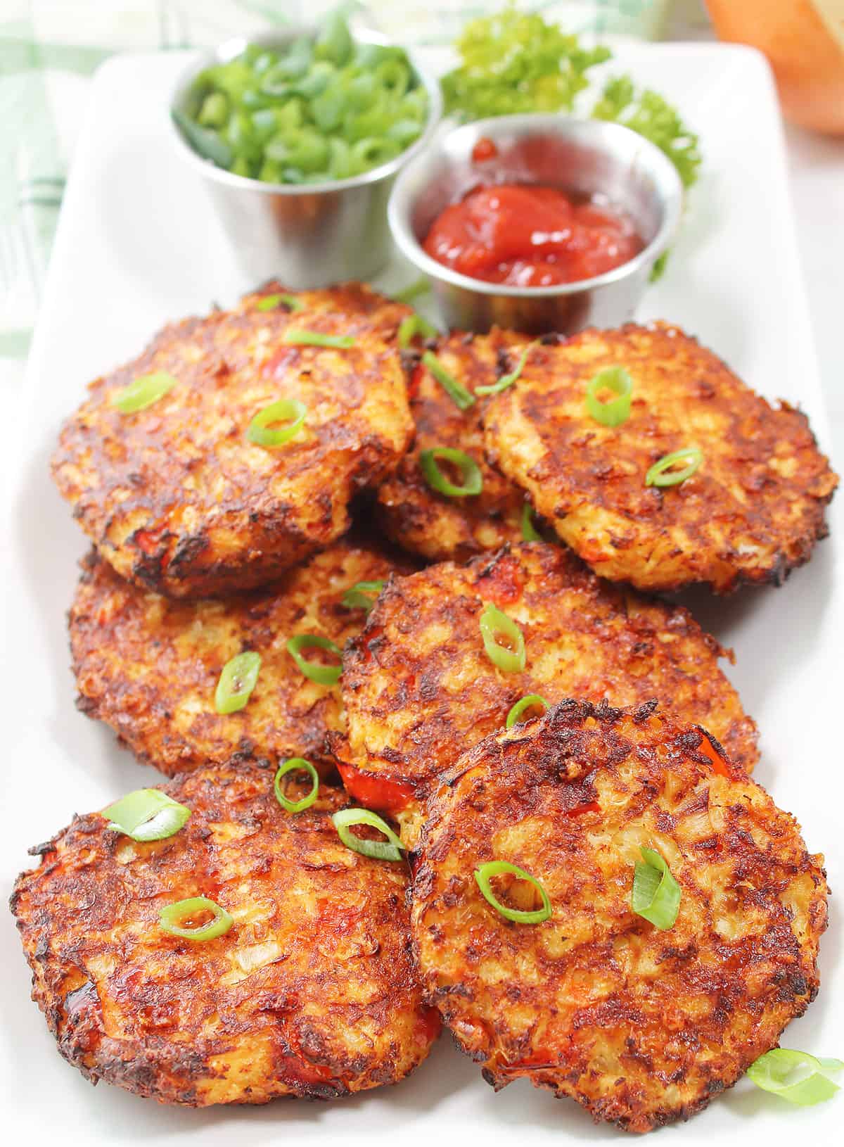 Closeup of air fryer cauliflower hash browns on platter with ketchup and green onions.