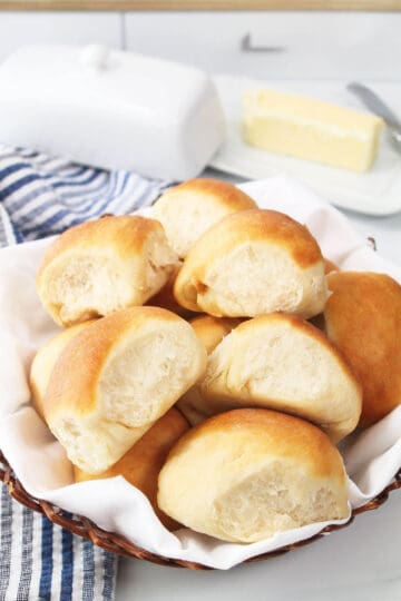 Dinner rolls in basket with butter dish in back.