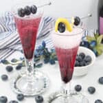 Two blueberry bellini cocktails with garnish.