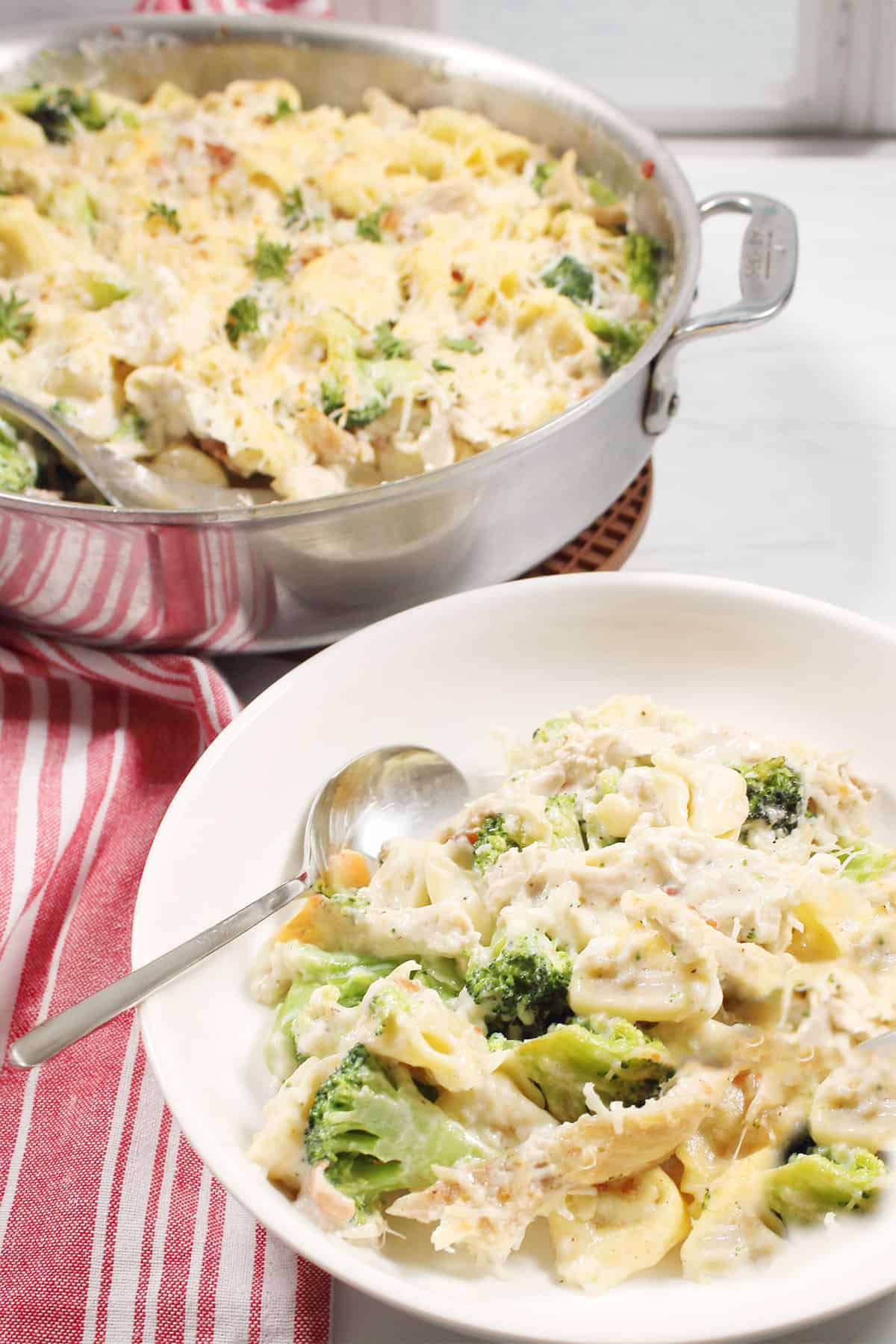 Serving of tortellini alfredo with chicken in front of pan.
