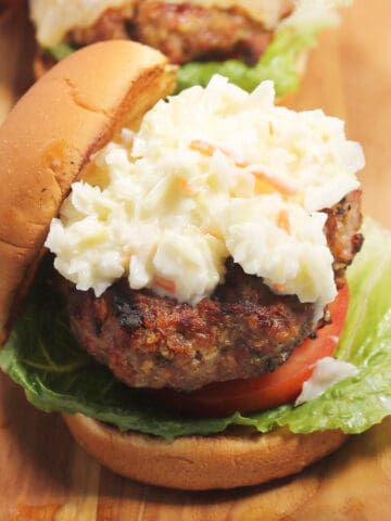 Closeup of grilled pork burger on bun with coleslaw.