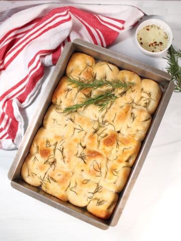 Focaccia Bread in pan with rosemary garnish.