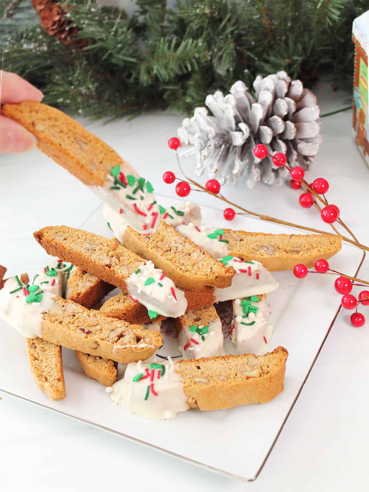 Grabbing a Gingerbread Biscotti from plate of white chocolate dipped biscotti.
