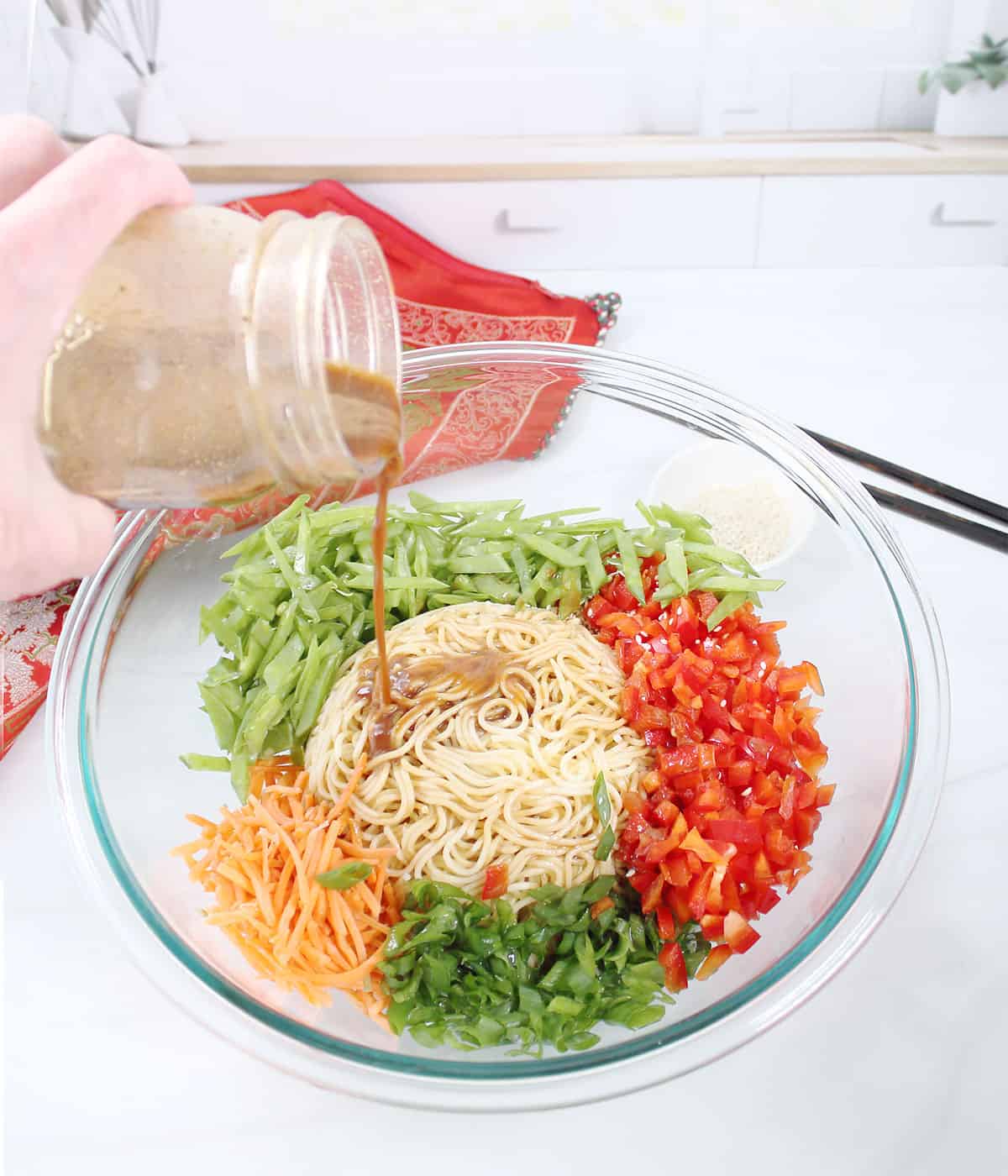 Pouring dressing over ingredients for noodle salad in bowl.