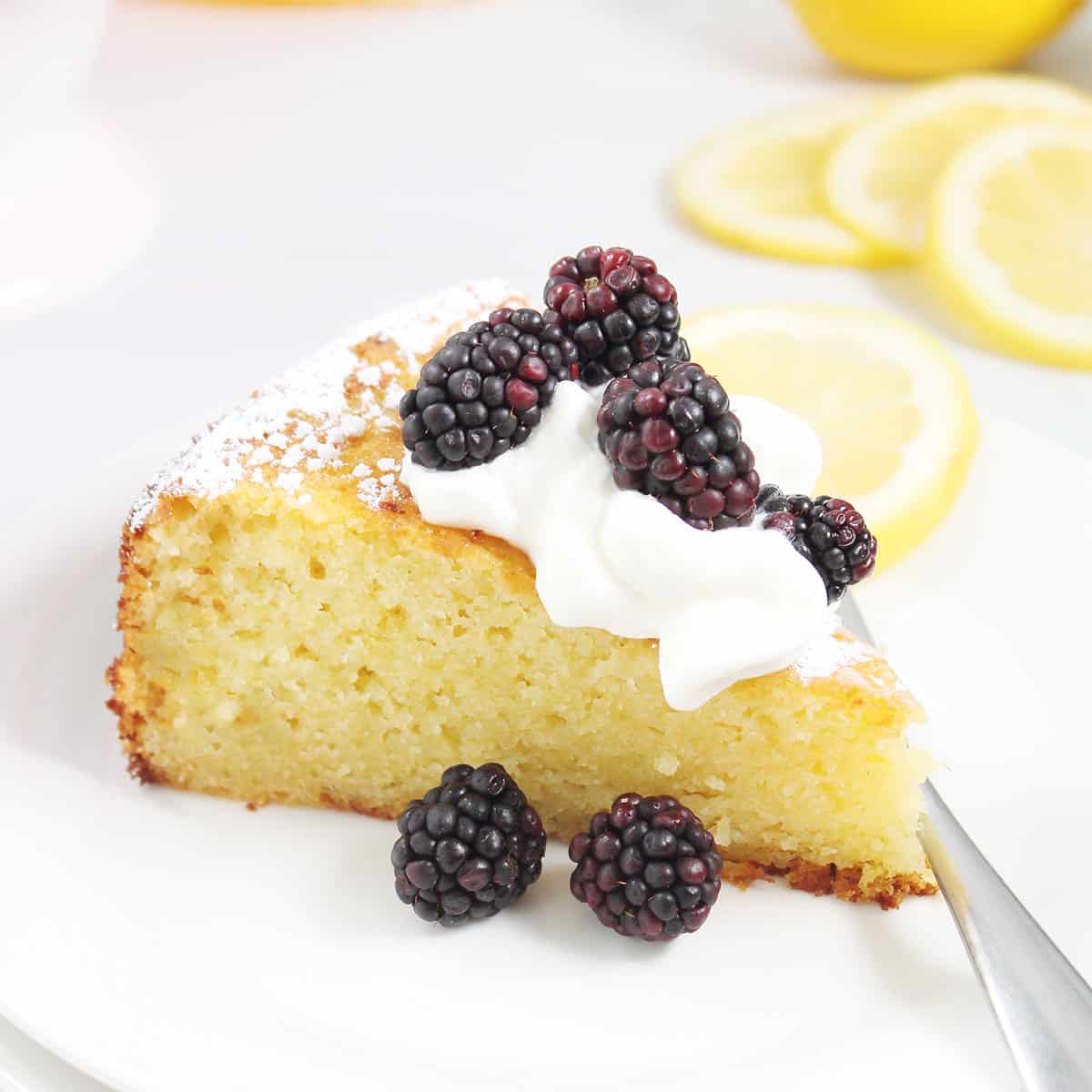 Slice of lemon ricotta cake with whipped cream and blackberries.