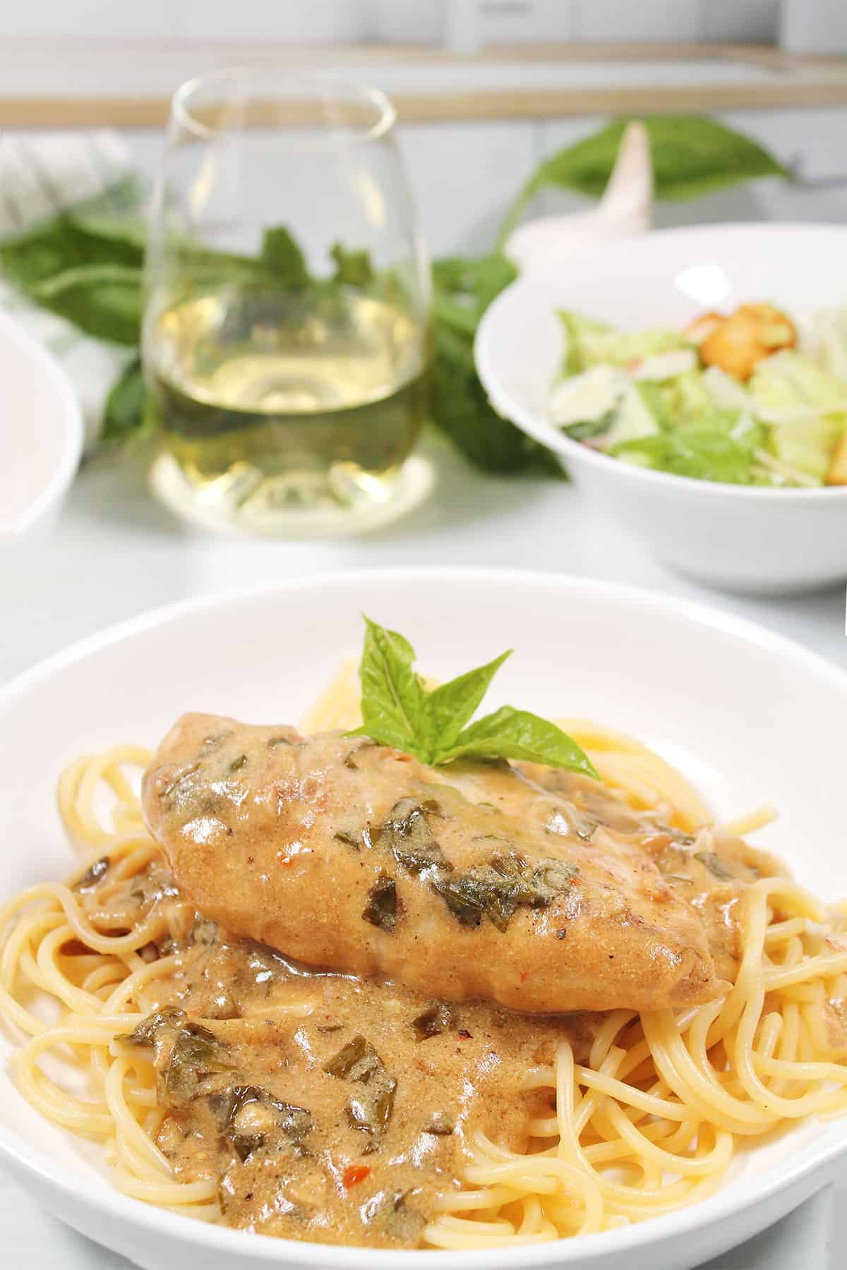 Chicken with Basil Cream Sauce plated over pasta.