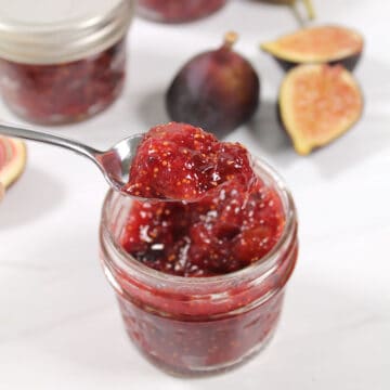 Spoonful of fig jam with fresh figs in back.