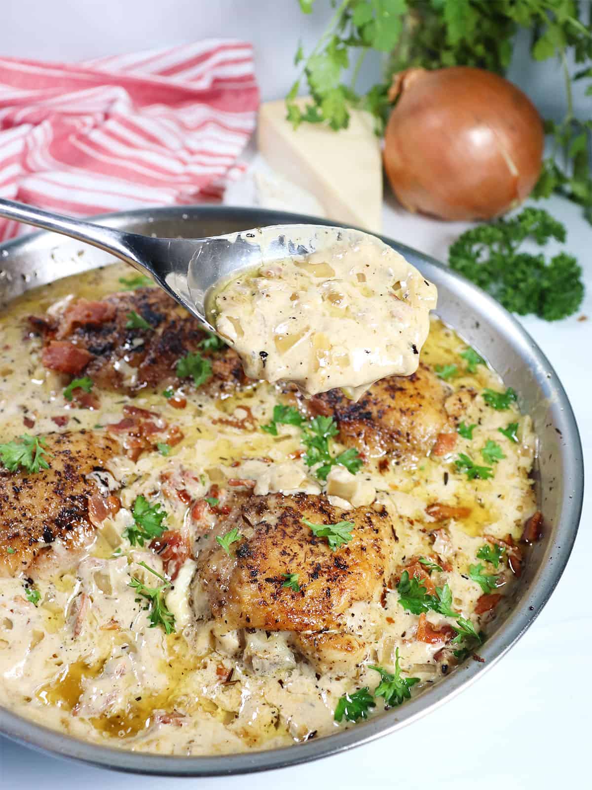 Drizzling sauce over Garlic Parmesan Chicken Thighs in skillet.