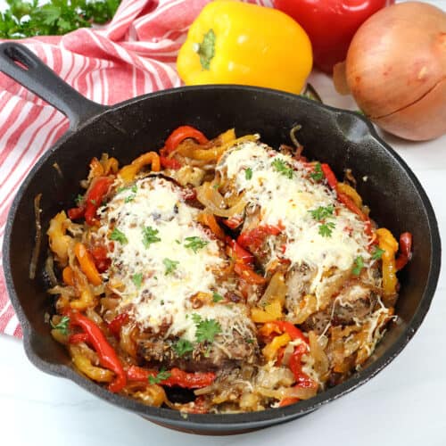 Hasselback Pork Tenderloins with peppers and onions in iron skillet.