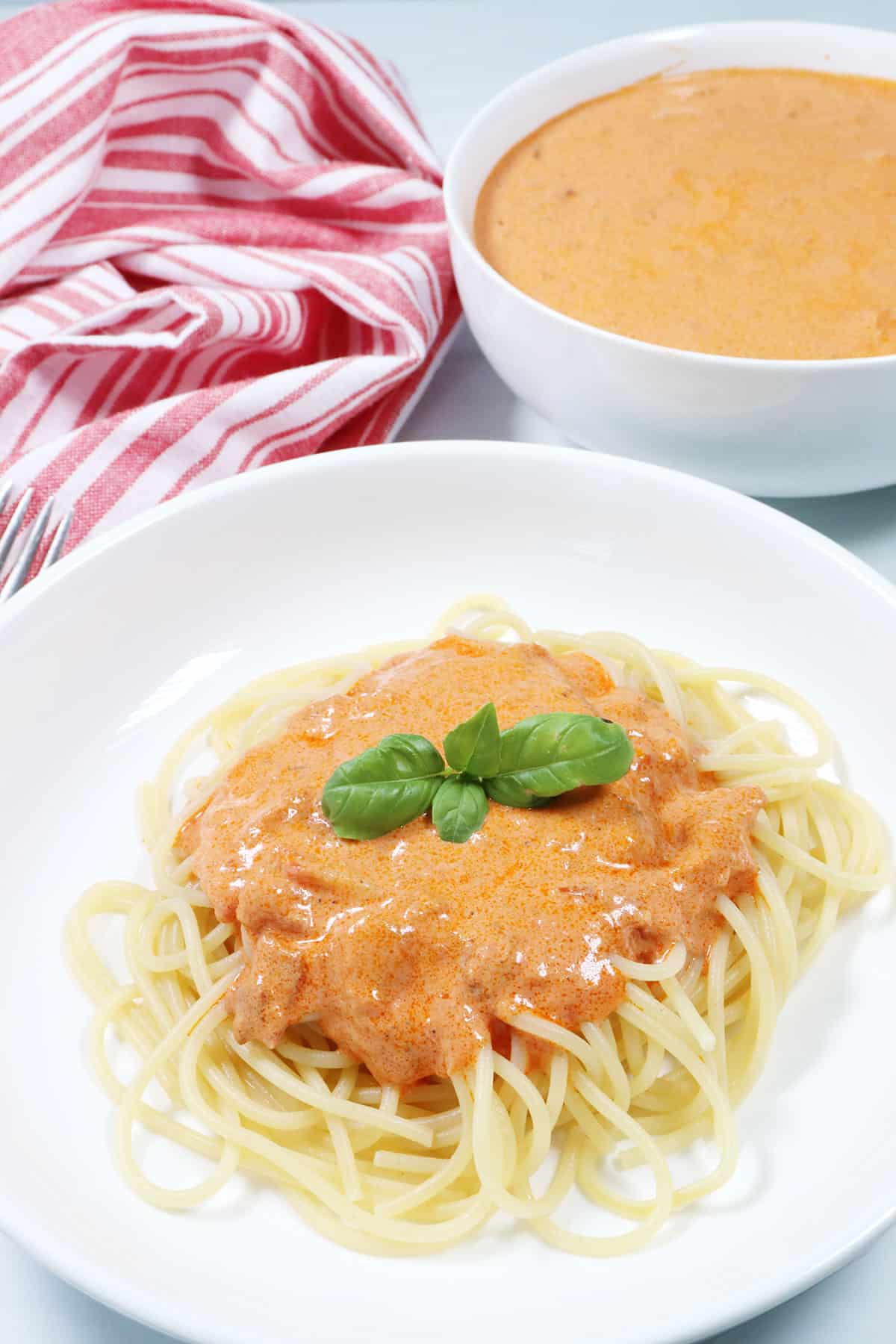 Easy Vodka Sauce recipe shown over pasta with bowl of sauce in back.